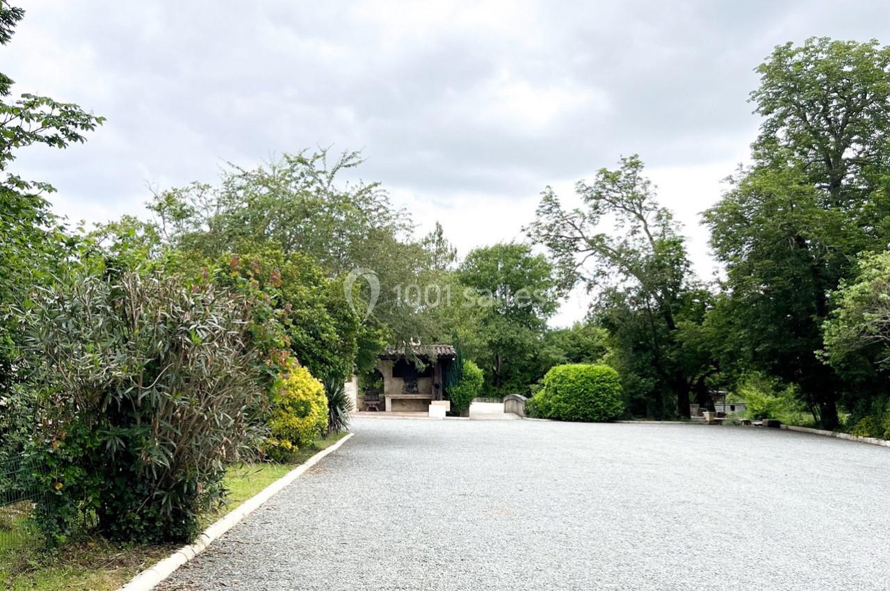 Allée en gravier bordée de végétation et menant à une petite structure en bois sous un ciel nuageux.