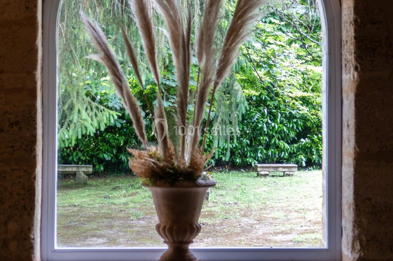 Vase décoratif avec des herbes de la pampa placé devant une fenêtre donnant sur un jardin verdoyant.