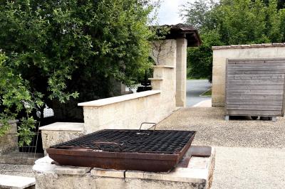 Barbecue en métal rouillé posé sur un socle en pierre, entouré de végétation et de murs en pierre.