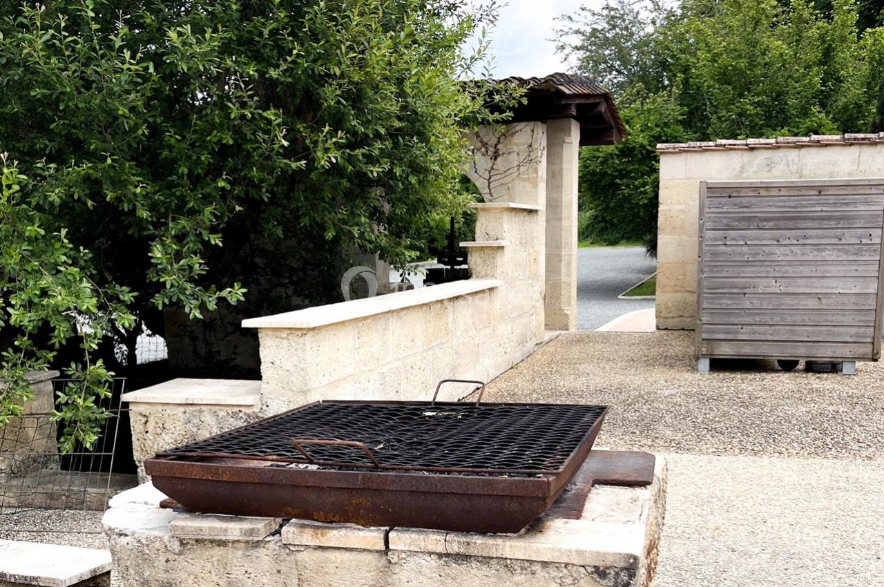 Barbecue en métal rouillé installé sur un muret en pierre, entouré d'arbres et de structures extérieures.