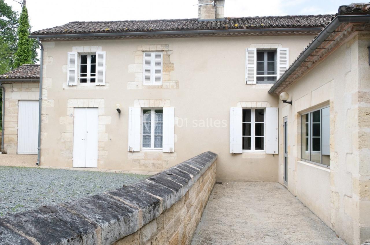 Façade d'une maison en pierre avec volets blancs, toit en tuiles et allée en gravier au premier plan.