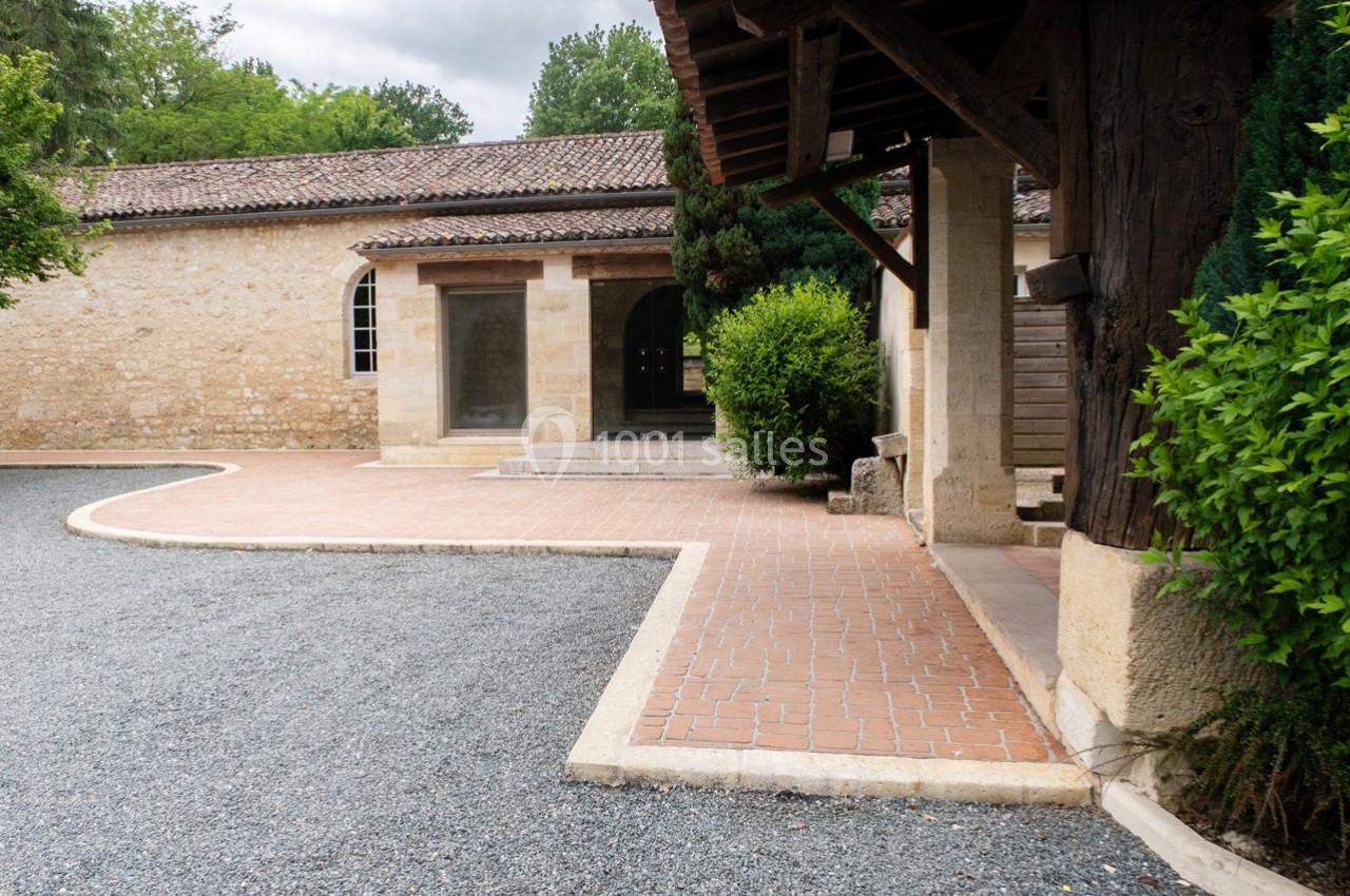 Allée pavée menant à une entrée voûtée en pierre, entourée de végétation et d'un bâtiment ancien.