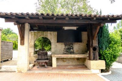 Barbecue en métal rouillé posé sur un socle en pierre, entouré de végétation et de murs en pierre.