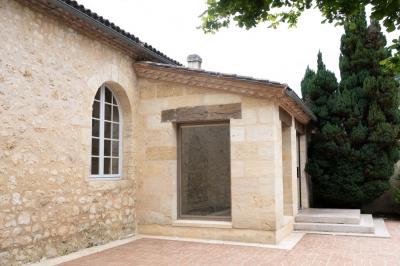Barbecue en métal rouillé posé sur un socle en pierre, entouré de végétation et de murs en pierre.