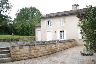 Barbecue en métal rouillé posé sur un socle en pierre, entouré de végétation et de murs en pierre.