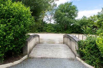 Barbecue en métal rouillé posé sur un socle en pierre, entouré de végétation et de murs en pierre.