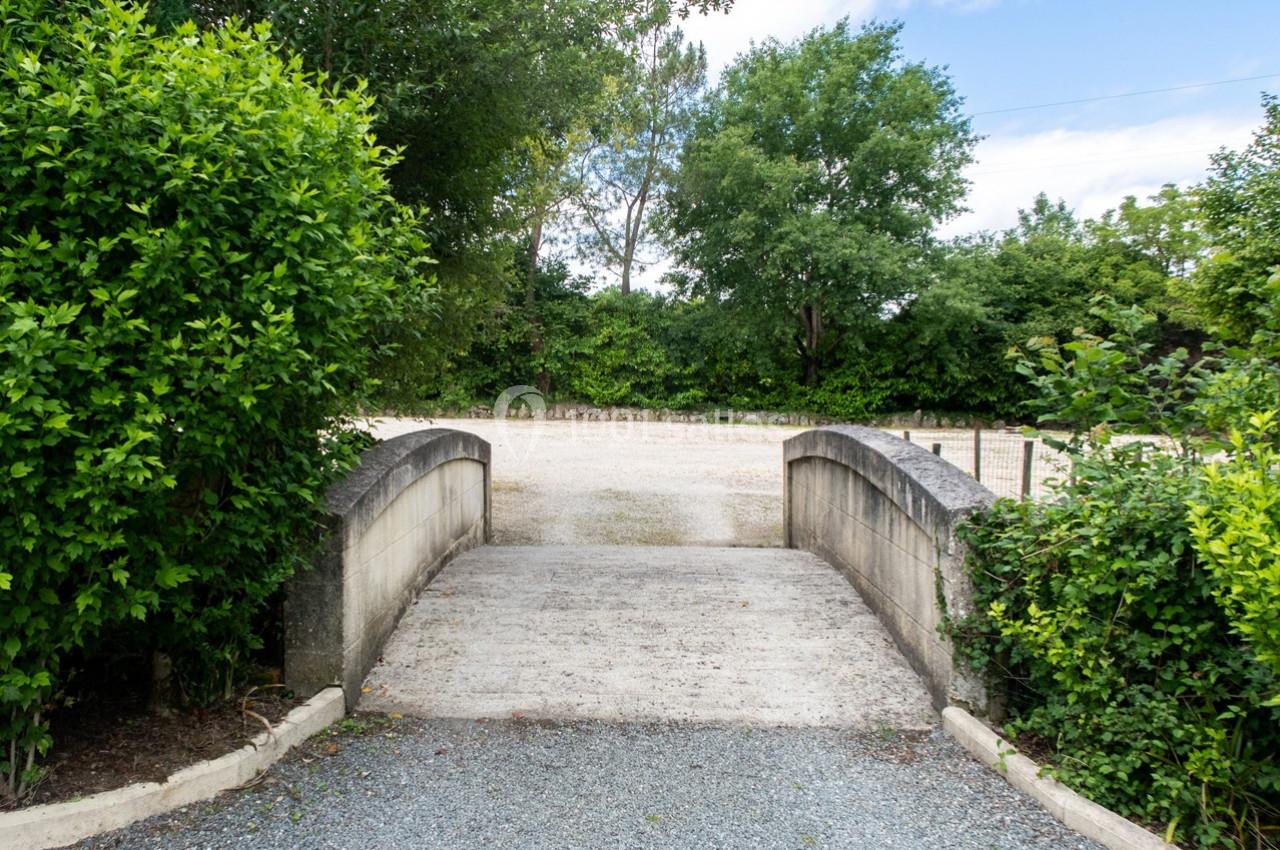 Petit pont en pierre traversant un chemin gravillonné, entouré de verdure et d'arbustes.