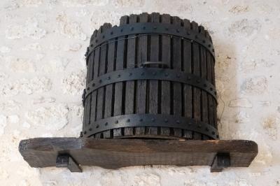 Barbecue en métal rouillé posé sur un socle en pierre, entouré de végétation et de murs en pierre.