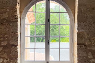 Barbecue en métal rouillé posé sur un socle en pierre, entouré de végétation et de murs en pierre.