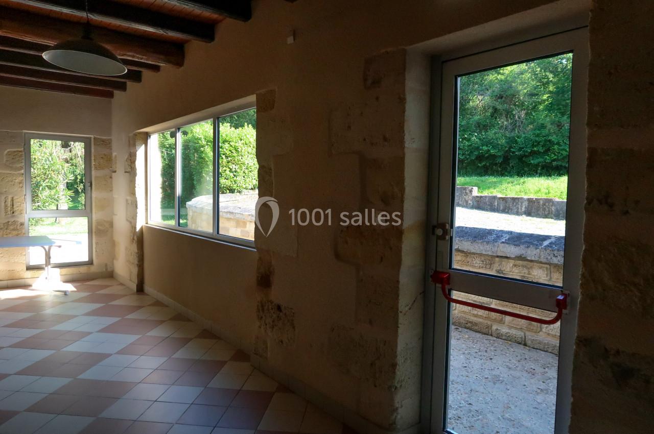 Intérieur d'une pièce avec murs en pierre, carrelage au sol, grandes fenêtres et une porte donnant sur un espace extérieur.