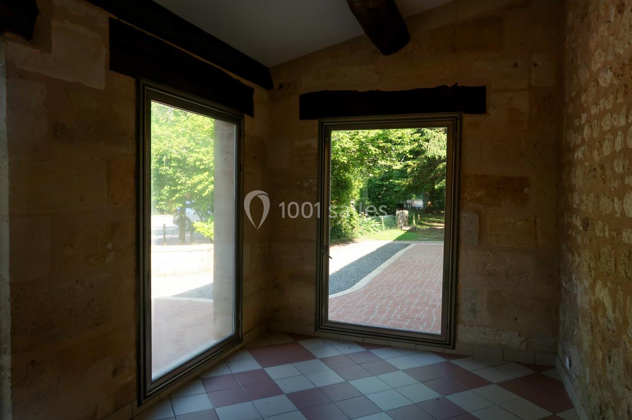 Deux grandes fenêtres laissent entrer la lumière dans une pièce aux murs en pierre et au sol carrelé.