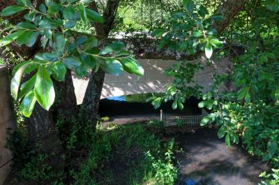 Barbecue en métal rouillé posé sur un socle en pierre, entouré de végétation et de murs en pierre.