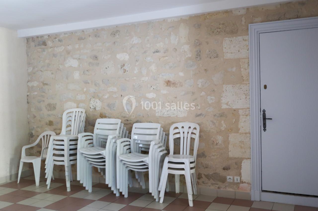 Chaises en plastique blanc empilées dans une pièce avec un mur en pierre et un sol carrelé.