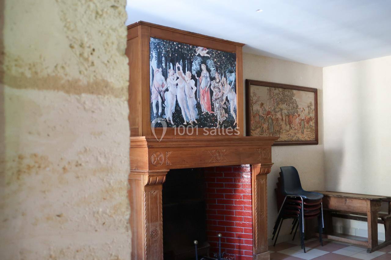 Cheminée en bois ornée d'une reproduction artistique, avec des chaises empilées et un mur en pierre à gauche.