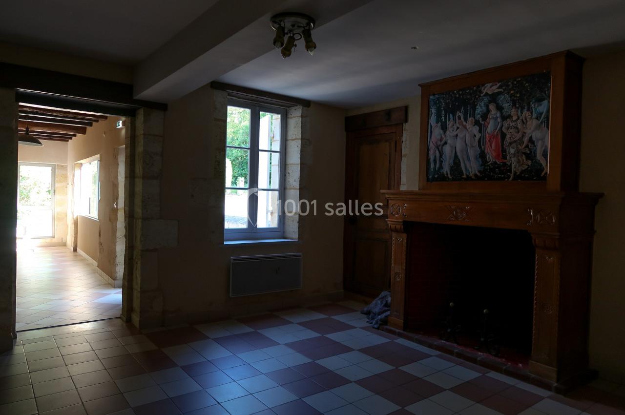 Une pièce vide avec cheminée en bois sculpté, carrelage au sol et lumière naturelle entrant par une fenêtre.