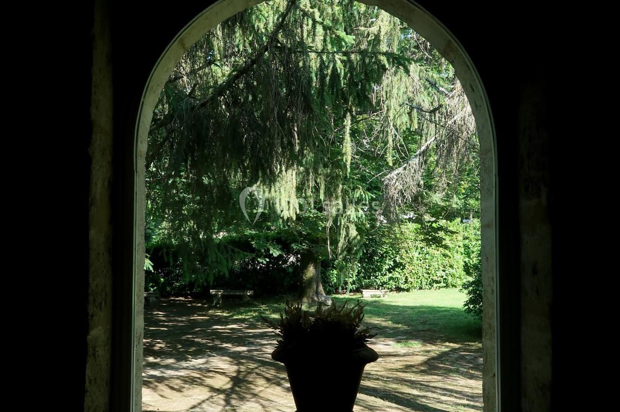 Vue d'un jardin verdoyant à travers une fenêtre en arche, avec une plante en pot au premier plan.
