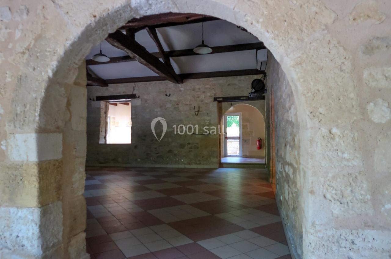 Intérieur d'une salle en pierre avec des arches, un sol carrelé et des poutres apparentes au plafond.