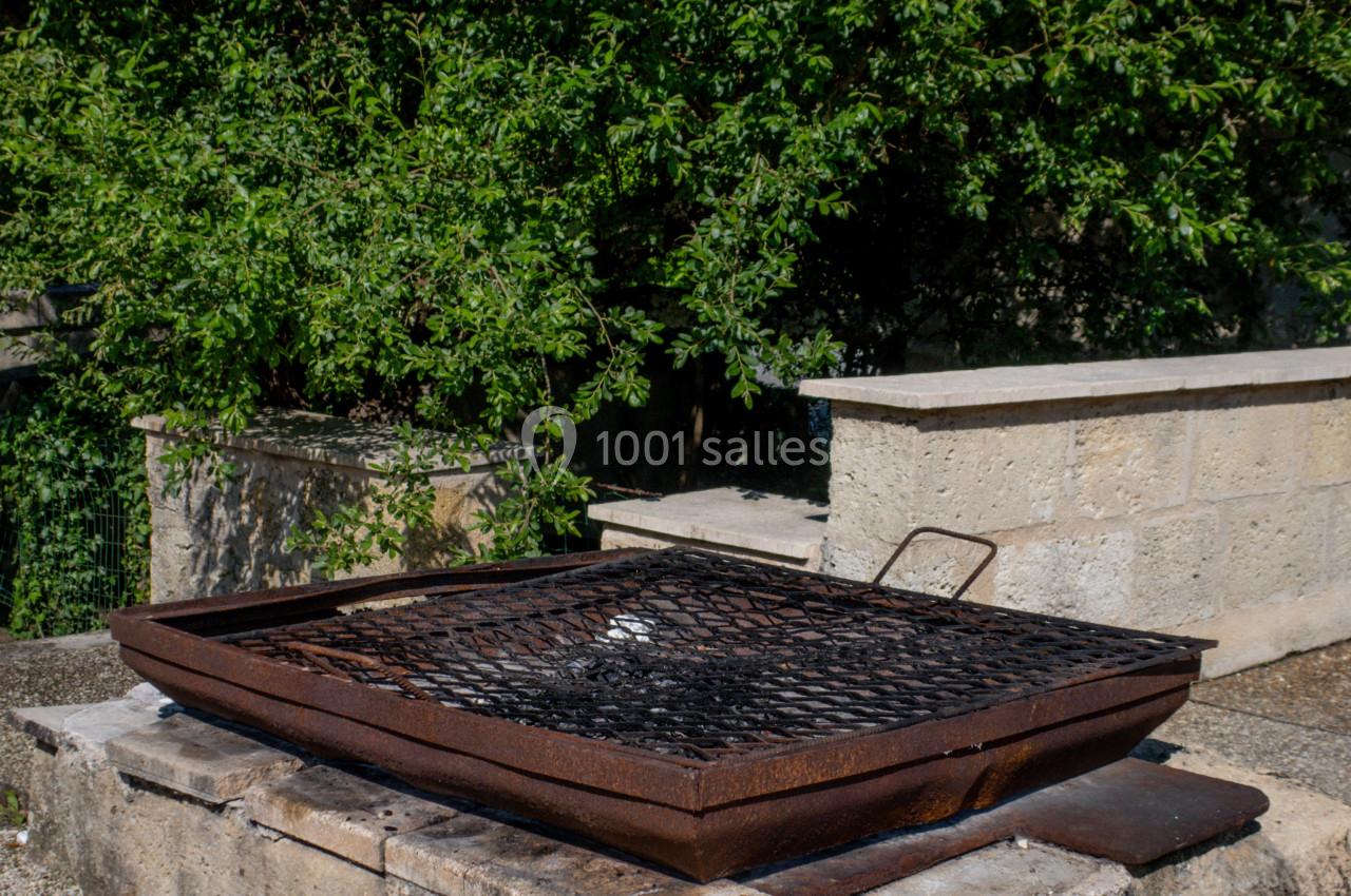 Barbecue en métal rouillé posé sur un socle en pierre, entouré de végétation et de murs en pierre.