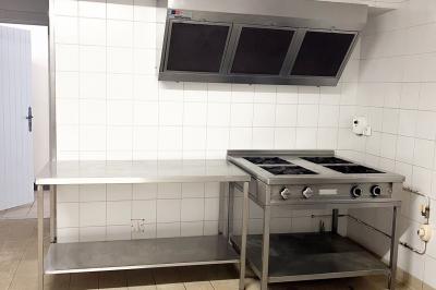 Barbecue en métal rouillé posé sur un socle en pierre, entouré de végétation et de murs en pierre.