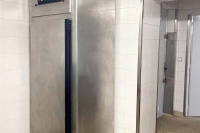 Barbecue en métal rouillé posé sur un socle en pierre, entouré de végétation et de murs en pierre.