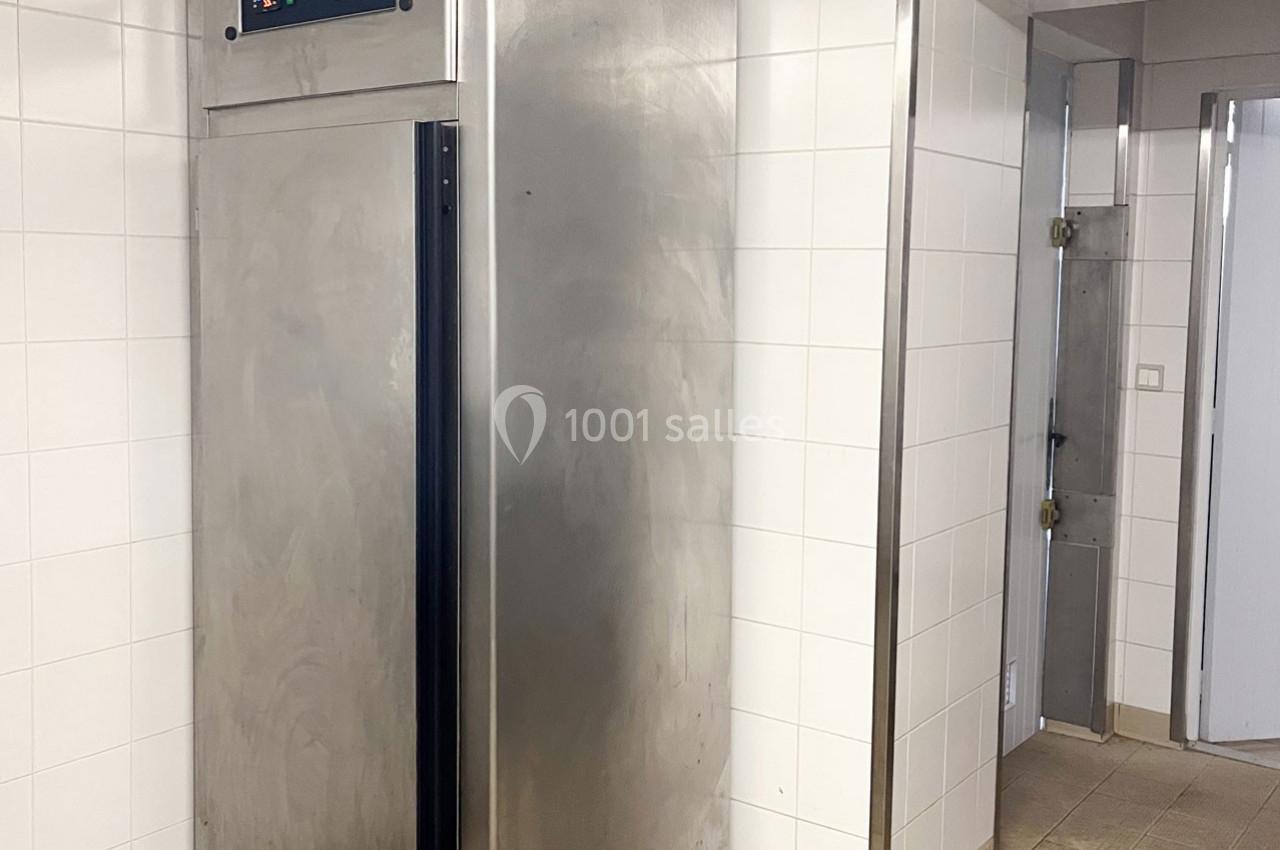 Armoire réfrigérée en acier inoxydable dans une pièce aux murs carrelés blancs et sol en carrelage beige.