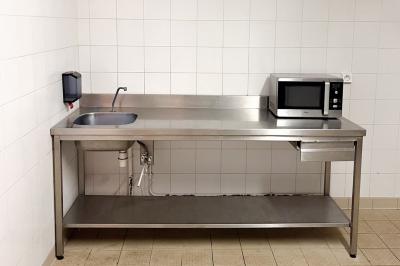 Barbecue en métal rouillé posé sur un socle en pierre, entouré de végétation et de murs en pierre.