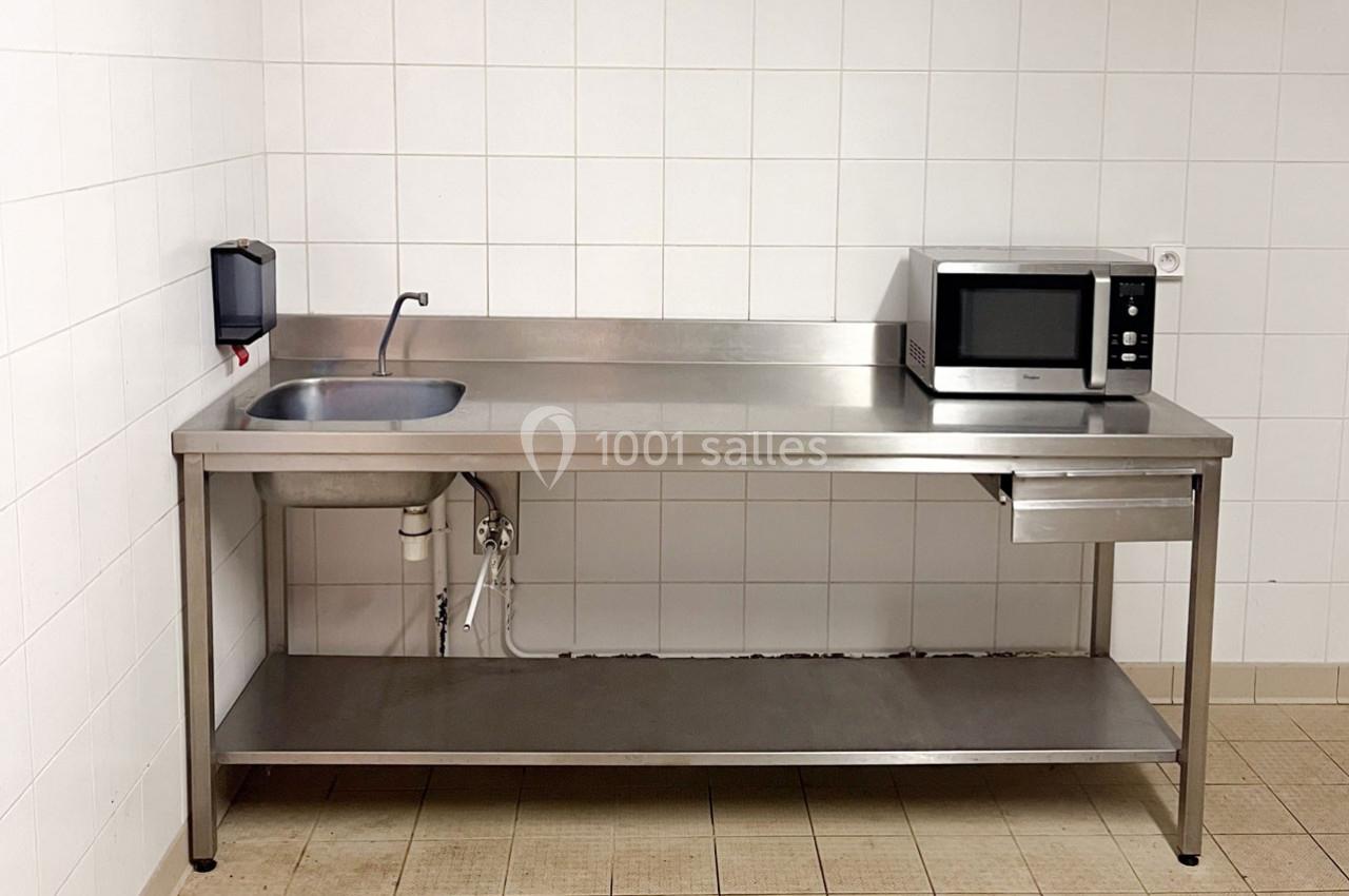 Évier en inox avec robinet, micro-ondes et plan de travail dans une cuisine aux murs carrelés blancs.