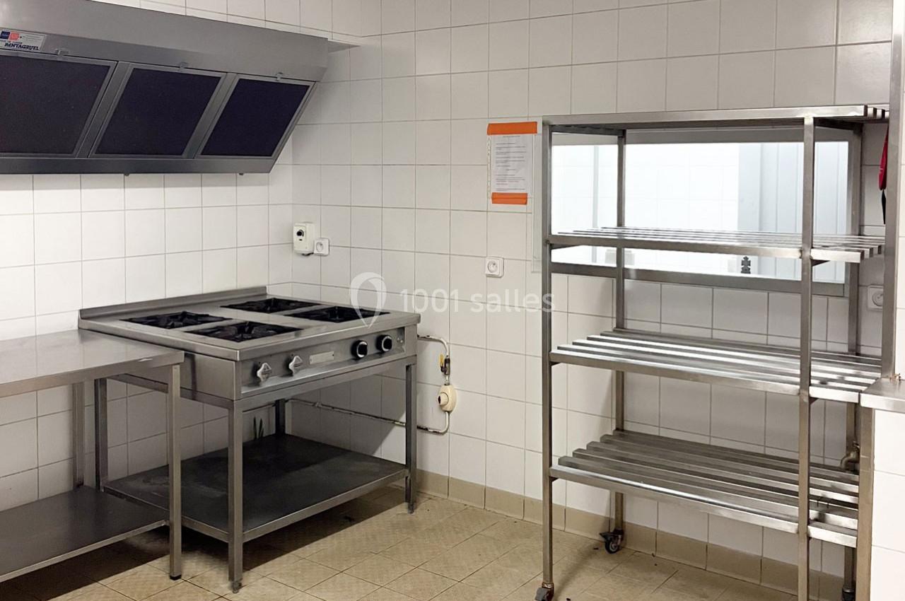 Cuisine professionnelle avec plaques de cuisson en inox, étagères métalliques et murs carrelés blancs.