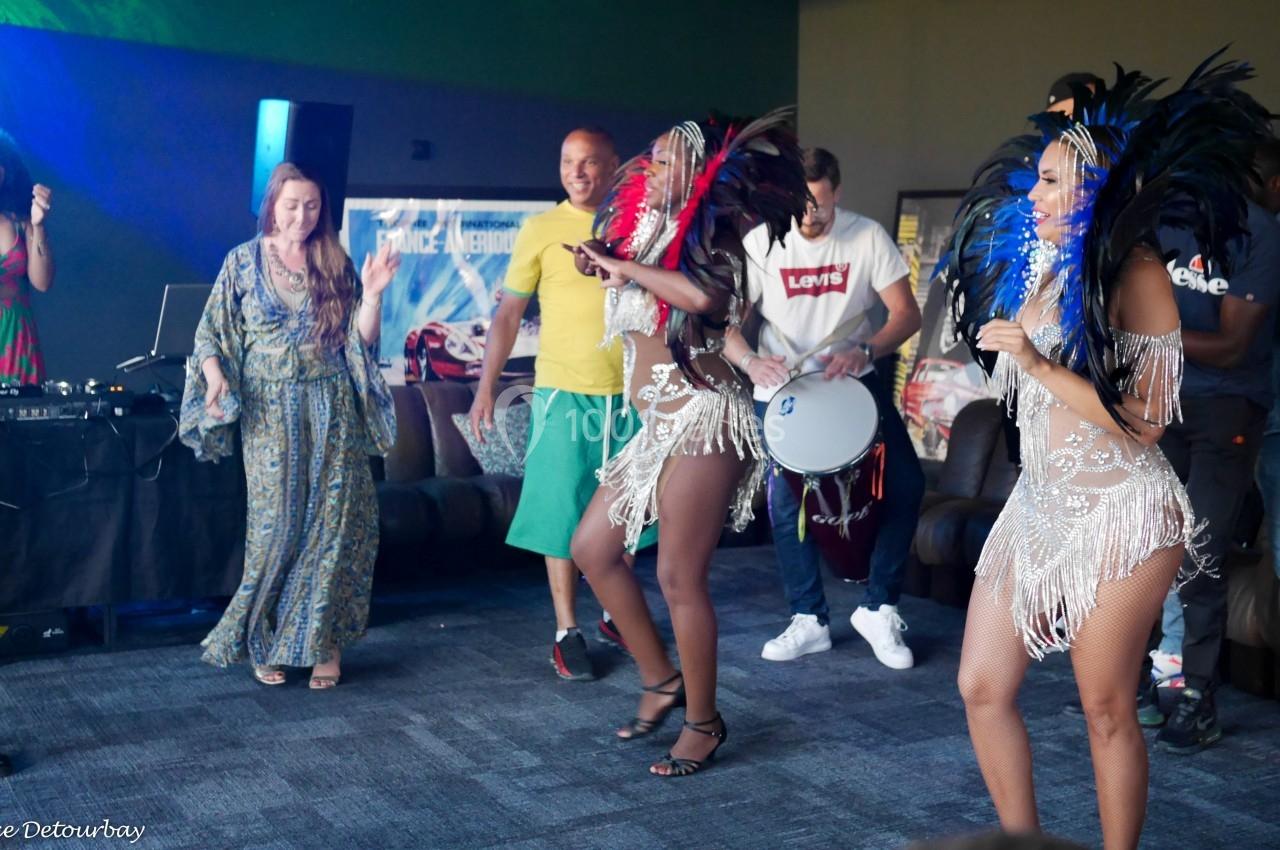 Des danseuses en costumes à plumes colorées se produisent devant un public dans une ambiance festive en intérieur.