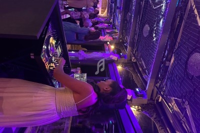 Une DJ anime une soirée dans un espace éclairé de lumières violettes, avec des invités dansant en arrière-plan.