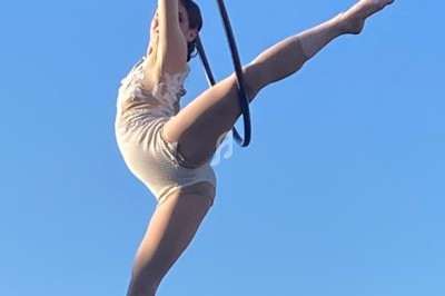 Une artiste exécute une figure aérienne sur un cerceau suspendu, en plein ciel dégagé.
