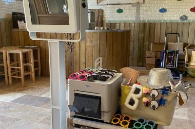 Borne photo avec accessoires festifs et imprimante, installée dans une pièce lumineuse au style rustique.