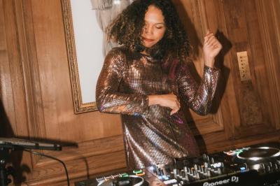 Une DJ mixant de la musique sur une table de mixage dans une ambiance lumineuse violette.