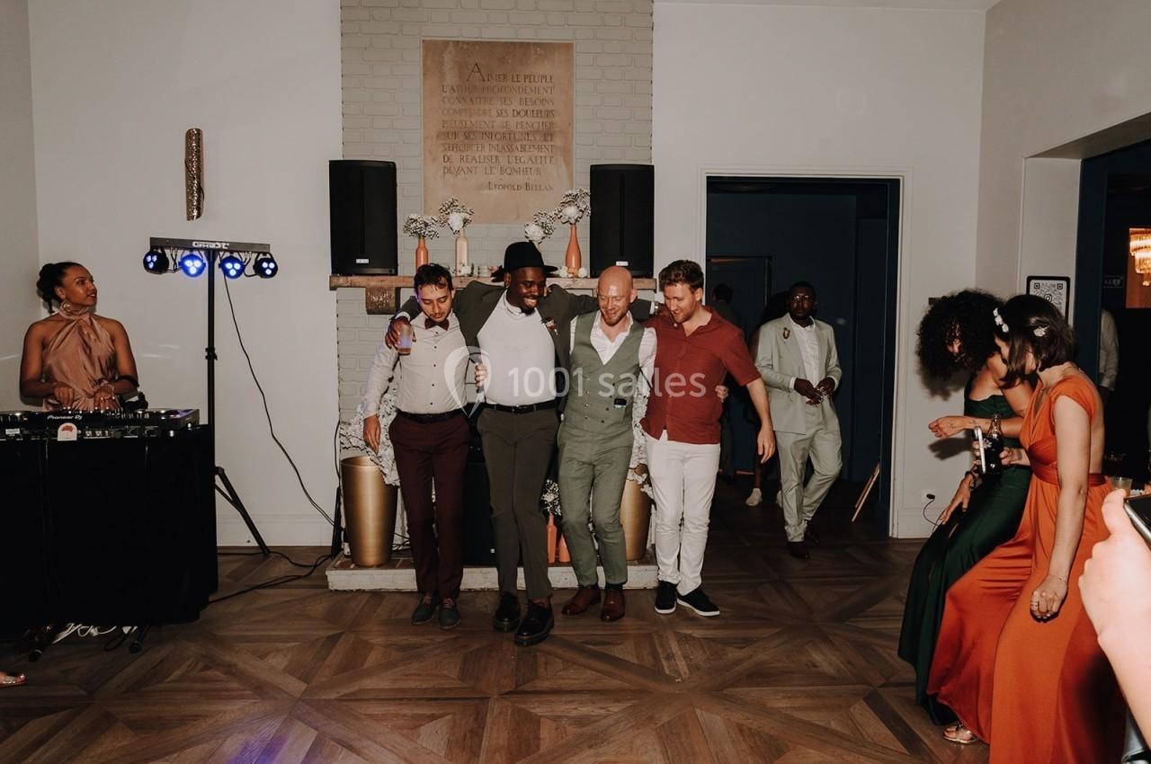 Des personnes dansent en groupe sur un parquet lors d'une fête, avec une DJ à gauche et des invités en arrière-plan.