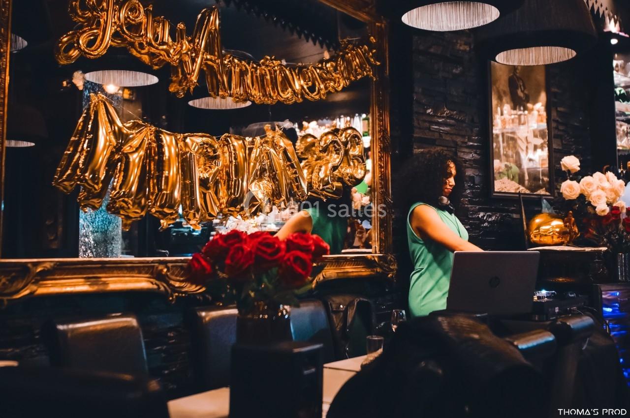 Une femme en robe verte se tient près d'un ordinateur dans une salle décorée avec des ballons dorés et des roses rouges.