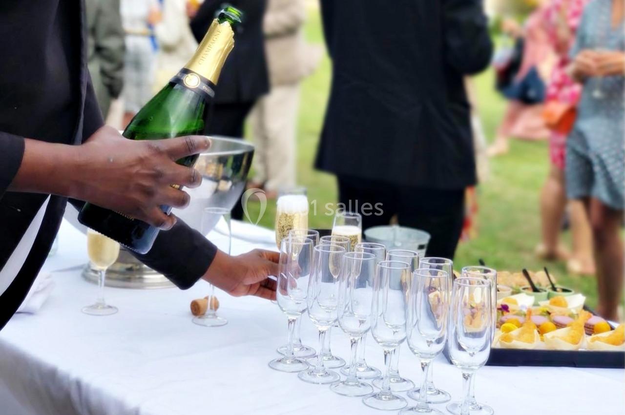 Un serveur remplit des flûtes de champagne sur une table lors d'un événement en extérieur.