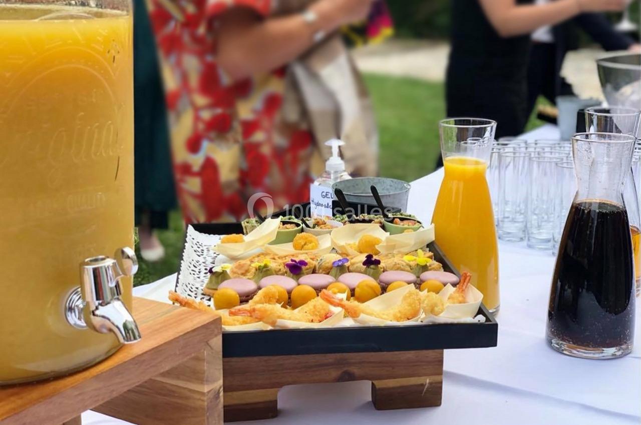 Buffet en extérieur avec jus de fruits, carafes et plateau de bouchées colorées décorées de fleurs comestibles.