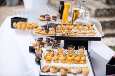 Table dressée en extérieur avec des plats, ustensiles de cuisine et présentoirs en bois devant une haie verte.