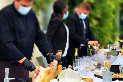 Table dressée en extérieur avec des plats, ustensiles de cuisine et présentoirs en bois devant une haie verte.