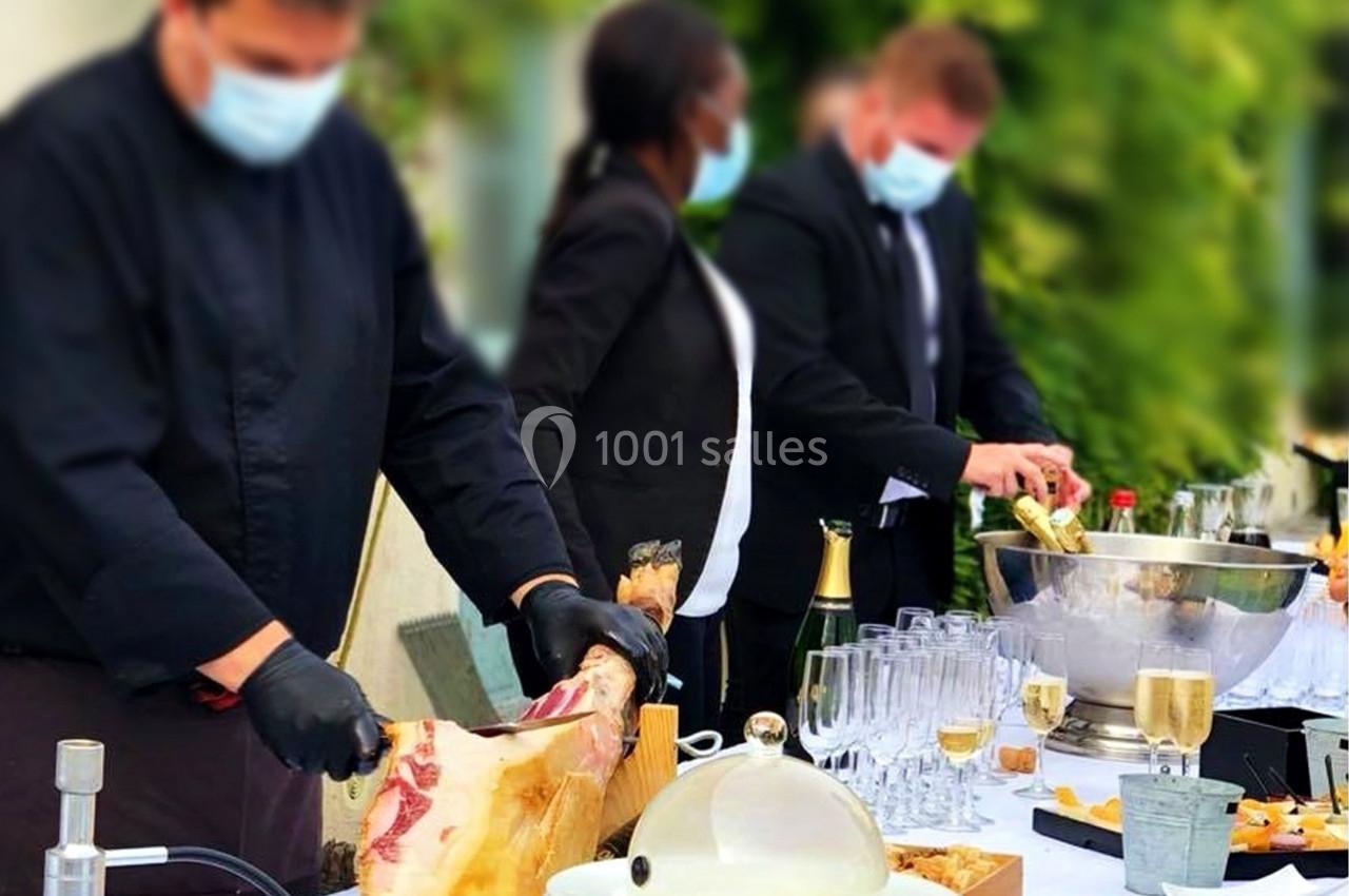Un chef découpe du jambon tandis que deux personnes servent des boissons lors d'un événement en extérieur.