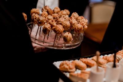 Table dressée en extérieur avec des plats, ustensiles de cuisine et présentoirs en bois devant une haie verte.