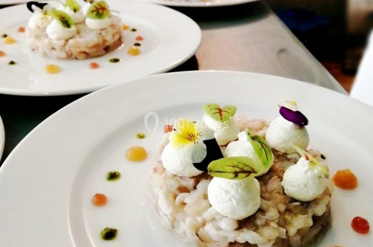 Assiette de risotto dressée avec des quenelles de fromage, des herbes fraîches et des fleurs comestibles.