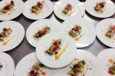 Table dressée en extérieur avec des plats, ustensiles de cuisine et présentoirs en bois devant une haie verte.