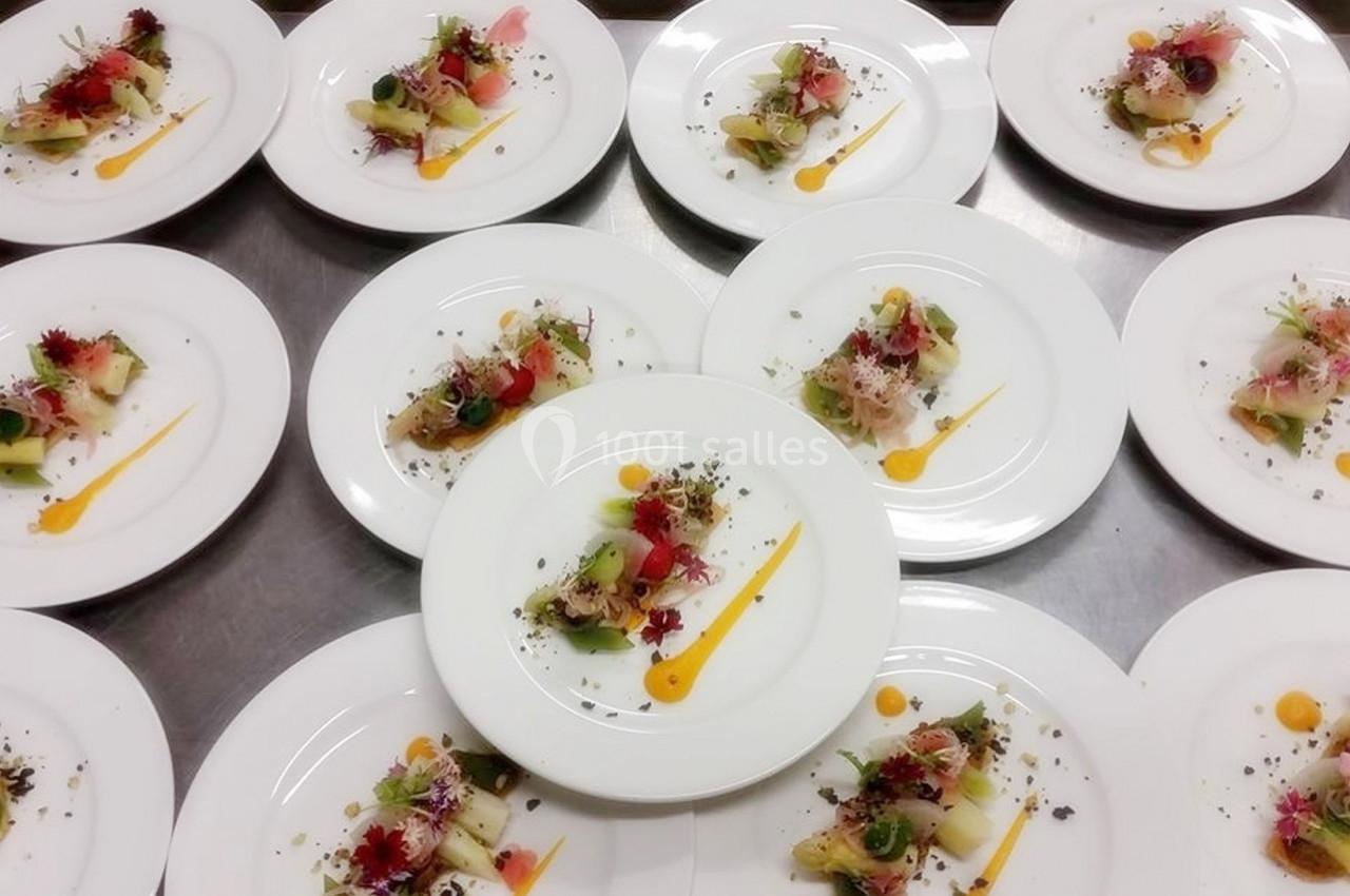 Assiettes dressées avec des portions de légumes colorés, sauce jaune et garnitures fines sur une table en inox.