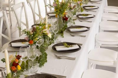 Table dressée en extérieur avec des plats, ustensiles de cuisine et présentoirs en bois devant une haie verte.