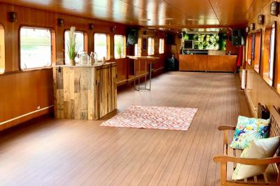 Intérieur d'une péniche avec parquet, bar en bois, tapis décoratif et grandes fenêtres donnant sur l'eau.