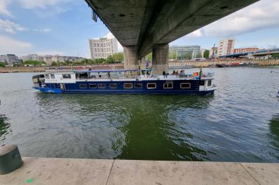 Intérieur d'une péniche avec parquet, bar en bois, tapis décoratif et grandes fenêtres donnant sur l'eau.