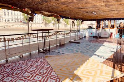 Intérieur d'une péniche avec parquet, bar en bois, tapis décoratif et grandes fenêtres donnant sur l'eau.