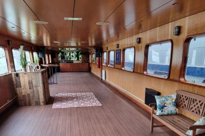 Intérieur d'une péniche avec parquet, bar en bois, tapis décoratif et grandes fenêtres donnant sur l'eau.