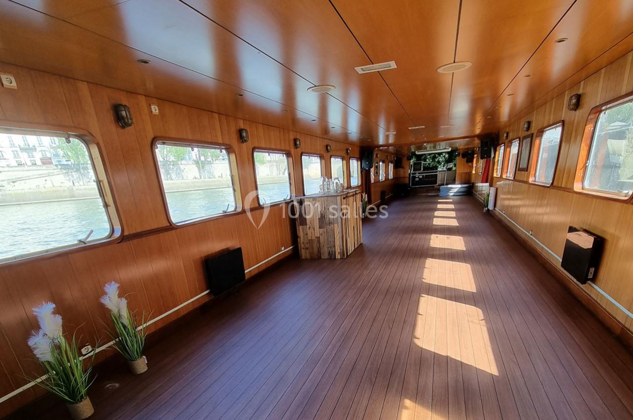 Intérieur d'une péniche avec parquet en bois, grandes fenêtres laissant entrer la lumière et quelques décorations simples.